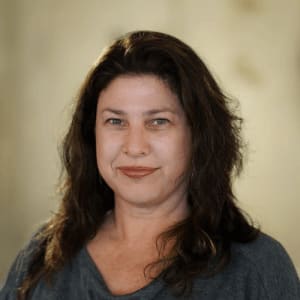 portrait of a woman with long dark hair smiling softly, neutral background emphasizing facial features and soft lighting