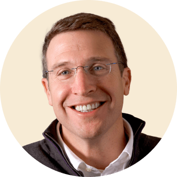 smiling man with glasses in a circular frame, portrait of a professional in a casual jacket against a neutral background