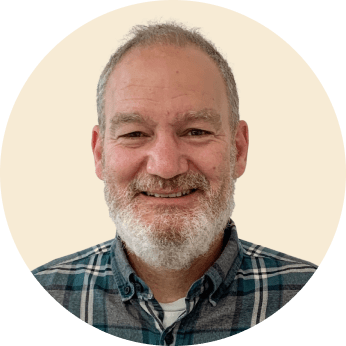 man with a white beard and smile wearing a plaid shirt against a neutral background, smiling man in circular frame portrait